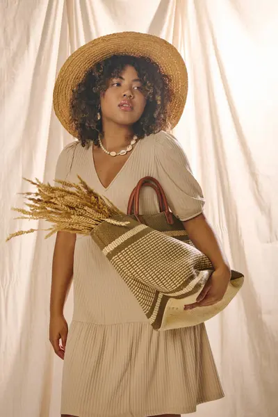 A beautiful young African American woman with curly hair wearing a straw hat and holding a purse in a studio setting. — Stock Photo