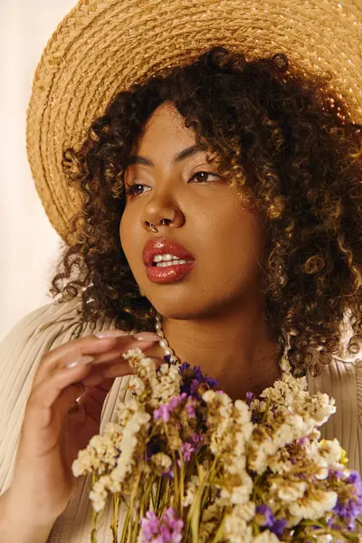 An elegant young African American woman with curly hair, wearing a straw hat, holds a vibrant bouquet of flowers. — Stock Photo