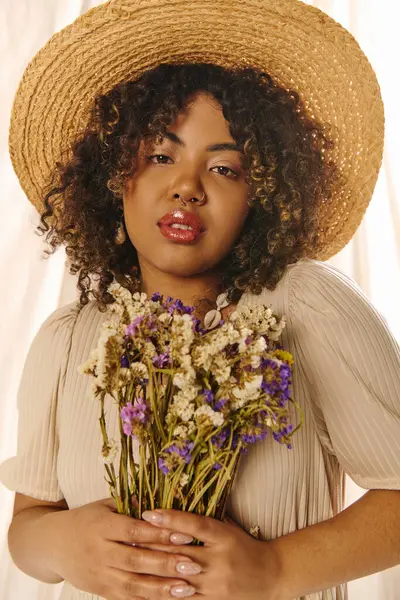 Une belle jeune femme afro-américaine aux cheveux bouclés et une robe d'été, tenant un bouquet de fleurs colorées. — Photo de stock