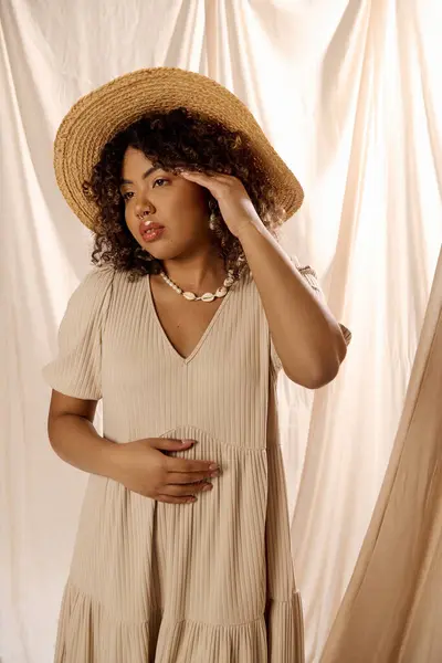 Uma bela jovem afro-americana com cabelo encaracolado posa em um vestido de verão e chapéu para uma sessão de fotos em um estúdio. — Fotografia de Stock