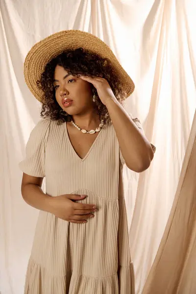 A beautiful young African American woman with curly hair poses in a summer dress and hat for a photoshoot in a studio setting. — Stock Photo