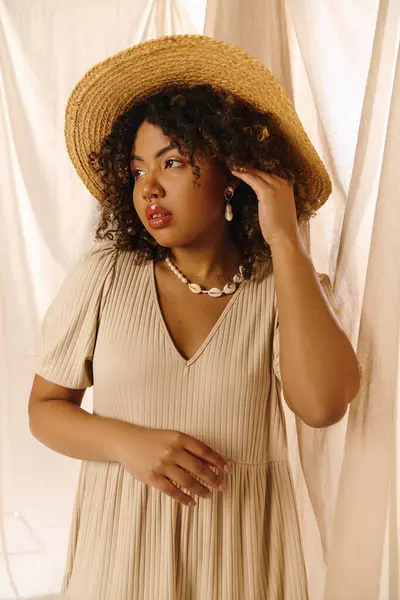 Une belle jeune femme afro-américaine aux cheveux bouclés pose gracieusement dans une robe d'été et un chapeau de paille. — Photo de stock