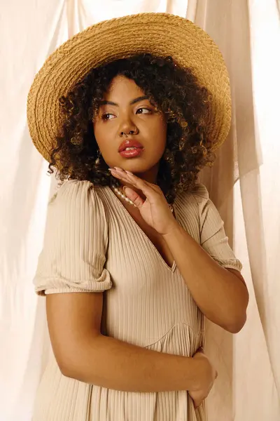 Uma bela jovem afro-americana com cabelo encaracolado posa graciosamente em um estúdio, usando um chapéu de palha e um vestido de verão.. — Fotografia de Stock