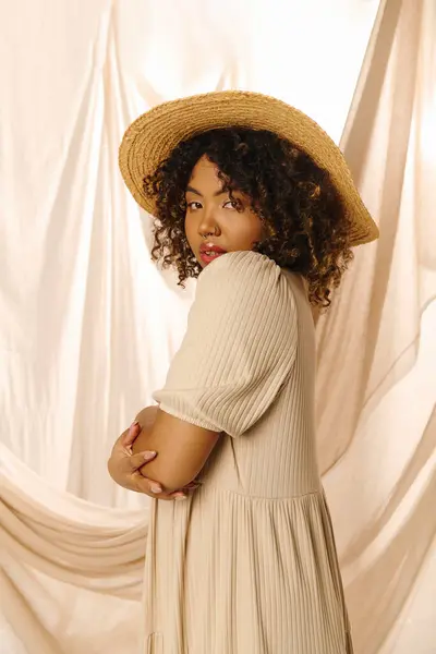 A beautiful young African American woman with curly hair wearing a hat and summer dress in a studio setting. — Stock Photo
