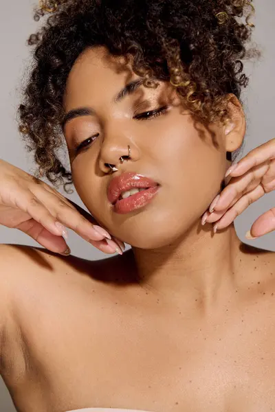 A beautiful young African American woman with curly hair touching her face while wearing a strapless top in a studio setting. — Stock Photo