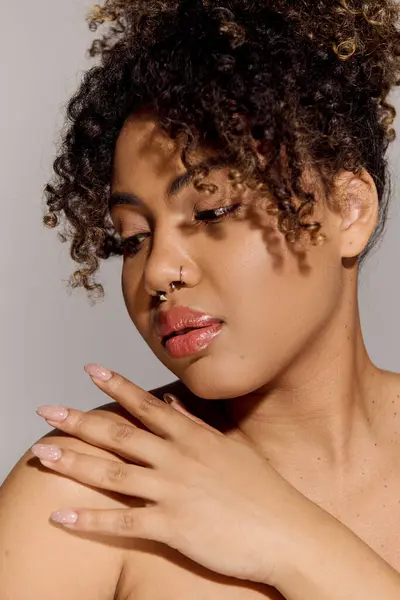 Молода афроамериканка з кучерявим волоссям, що стоїть в студії, обережно кладе руку на її груди сердечним жестом. — стокове фото