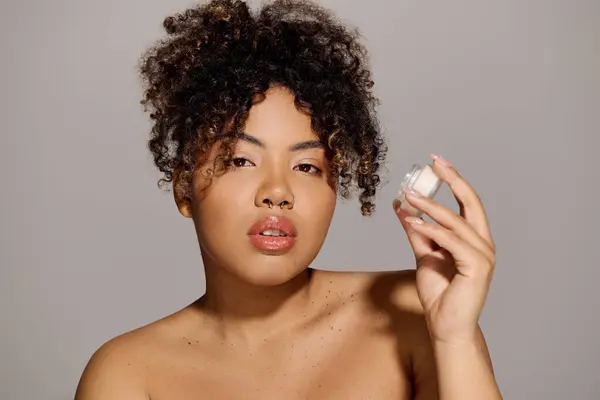 Молодая афроамериканка с кудрявыми волосами держит банку крема для лица — стоковое фото