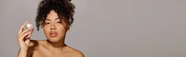 Young African American woman with curly hair holding jar of cream — Stock Photo