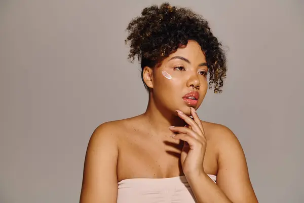 Young African American woman with curly hair, peacefully holds hand to face in a studio setting. — Stock Photo