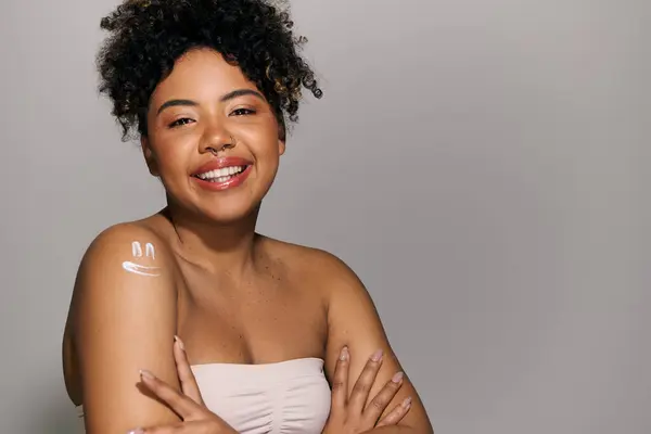 A beautiful young African American woman with curly hair poses confidently, crossing her arms for a portrait in a studio setting. — Stock Photo