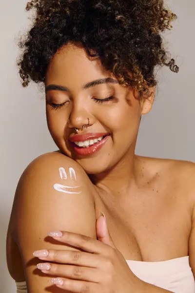 A beautiful young African American woman with curly hair smiling while her arm beams with radiance in a studio setting. — Stock Photo