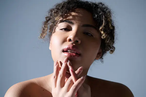 A beautiful young African American woman with curly hair, thoughtful expression, and hand on her mouth in a studio setting. — Stock Photo