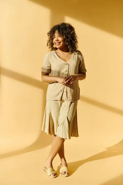 A beautiful young African American woman with curly hair standing tall in a room with a bright yellow wall. — Stock Photo