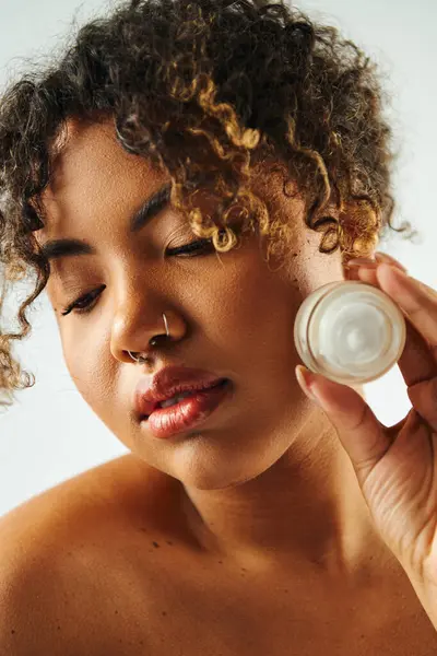 African American woman showcasing cream jar. — Stock Photo