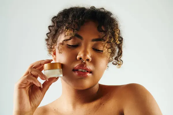 Mulher afro-americana graciosamente aplica creme em seu rosto. — Fotografia de Stock