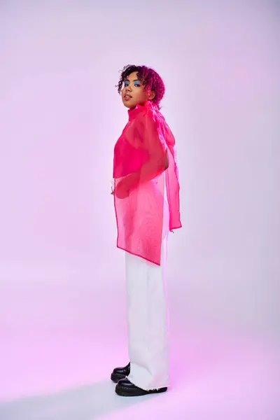 African American woman in pink shirt and white pants posing on vibrant backdrop. — Stock Photo