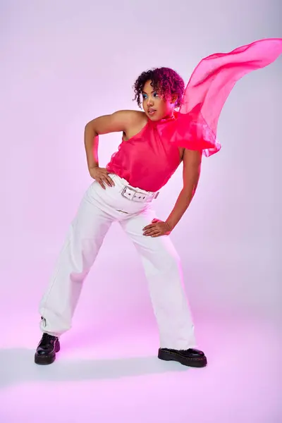 African American woman poses gracefully in white pants and pink shirt on vibrant backdrop. — Stock Photo