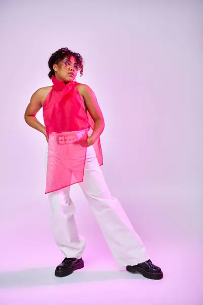 Eine Afroamerikanerin posiert selbstbewusst in rosa Hemd und weißer Hose vor einer lebendigen Kulisse. — Stockfoto