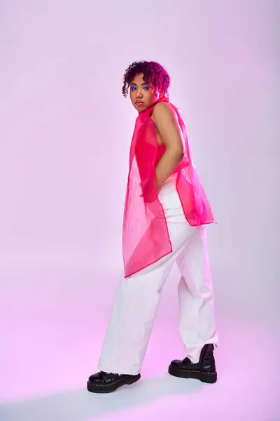 A beautiful African American woman poses actively in a pink top and white pants against a vibrant backdrop. — Stock Photo