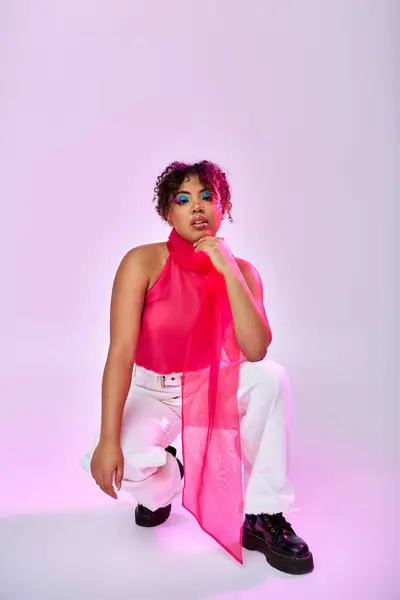 Una vibrante mujer afroamericana posando en un top rosa y pantalones blancos sobre un colorido telón de fondo. - foto de stock