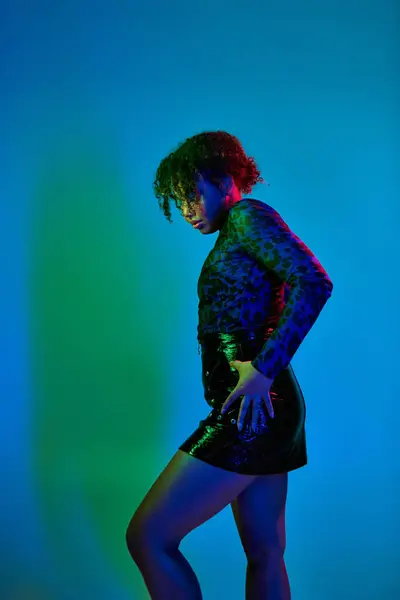 A stunning African American woman strikes a pose in a chic black dress against a vibrant backdrop. — Stock Photo