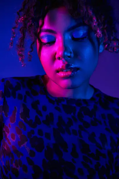 Uma mulher afro-americana impressionante com olhos azuis vestindo uma camisa de impressão de leopardo posa contra um cenário vibrante. — Fotografia de Stock