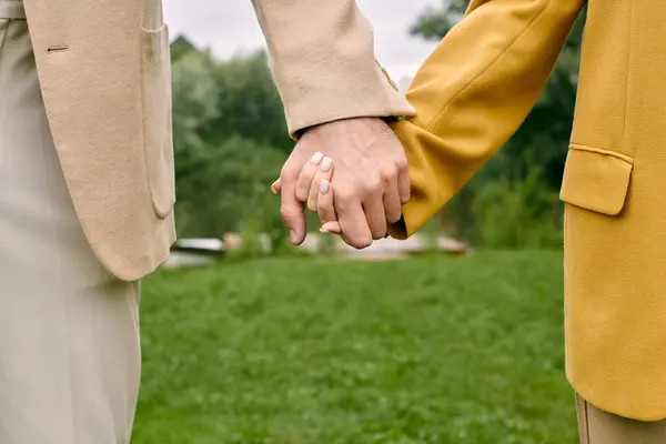 A close-up of two people, a beautiful couple, holding hands tenderly in a green park, showcasing love and connection. — Stock Photo