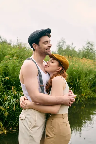 Um homem e uma mulher estão graciosamente juntos por um tranquilo corpo de água em um exuberante parque verde, compartilhando um momento romântico. — Fotografia de Stock