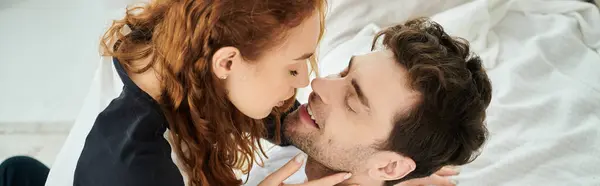 Мужчина нежно целует женщину в щеку, выражая любовь и привязанность в уютной спальне. — стоковое фото