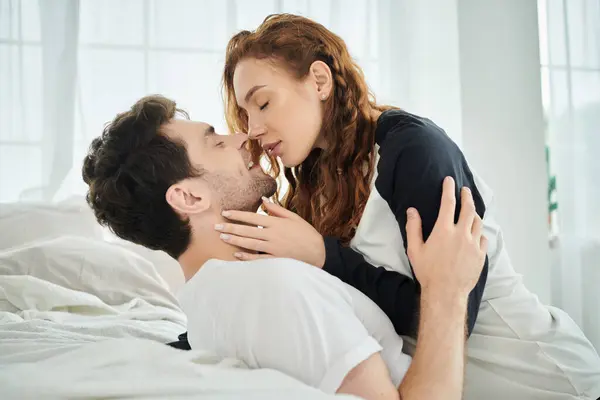 Ein Mann küsst eine Frau zärtlich auf die Wange und drückt damit Liebe und Intimität in einer gemütlichen Schlafzimmeratmosphäre aus. — Stockfoto