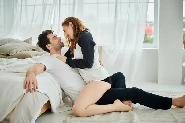 A man and woman sit on a bed, sharing a quiet moment together in a cozy bedroom setting. — Stock Photo