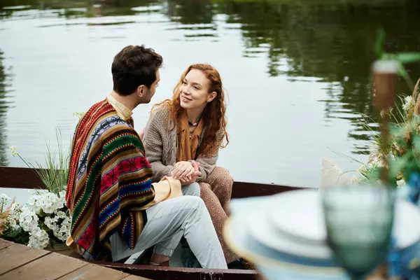 Ein Mann und eine Frau in Boho-Kleidung sitzen friedlich in einem Boot auf einem ruhigen See inmitten eines üppig grünen Parks. — Stockfoto