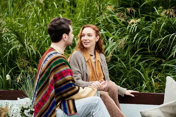 Un homme et une femme vêtus de vêtements de style boho sont assis sur un banc, engagés dans une conversation dans un cadre verdoyant parc. — Photo de stock