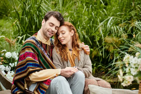 Um homem e uma mulher, ambos vestidos com roupas de estilo boho, sentam-se juntos em um parque verde, compartilhando um momento romântico.. — Fotografia de Stock
