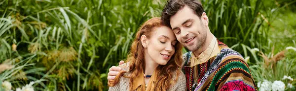 Un homme et une femme, vêtus de vêtements de style boho, se tenant ensemble dans un parc verdoyant, partageant un moment romantique. — Photo de stock