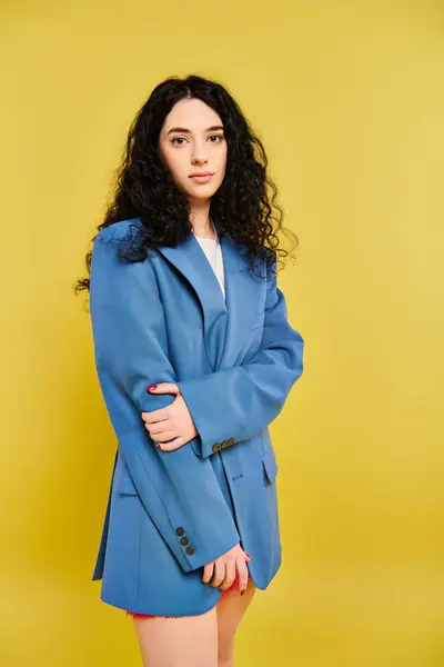 A stylish, young brunette woman with curly hair poses against a vibrant yellow background, exuding confidence and personality. — Stock Photo