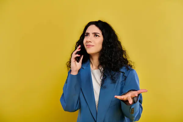 Una giovane donna bruna in giacca blu, che parla al cellulare, mostra lo stile e la connettività moderna su uno sfondo giallo. — Foto stock