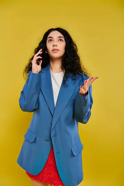 Bruna donna con i capelli ricci in posa in elegante giacca blu, in mostra le sue emozioni in uno studio con uno sfondo giallo. — Foto stock