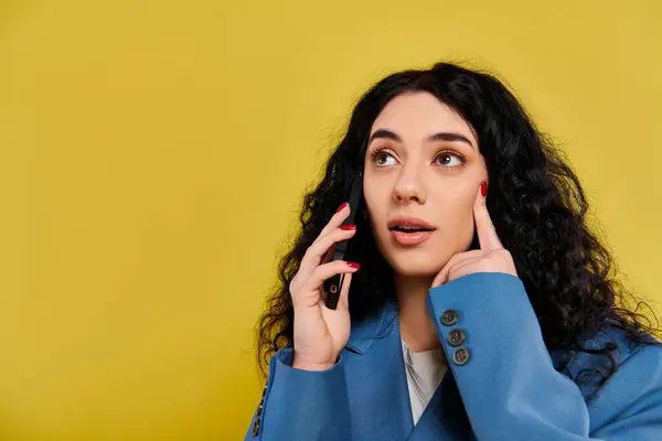 Young brunette woman in blue jacket, expressing emotion in studio with yellow background. — Stock Photo