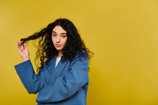 Una giovane donna elegante con i capelli ricci in posa di fronte a uno sfondo giallo vibrante, trasudando fiducia e fascino. — Foto stock