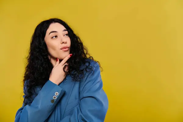 A young, curly-haired woman in a blue jacket exudes elegance and emotion as she poses in a studio with a yellow background. — Stock Photo