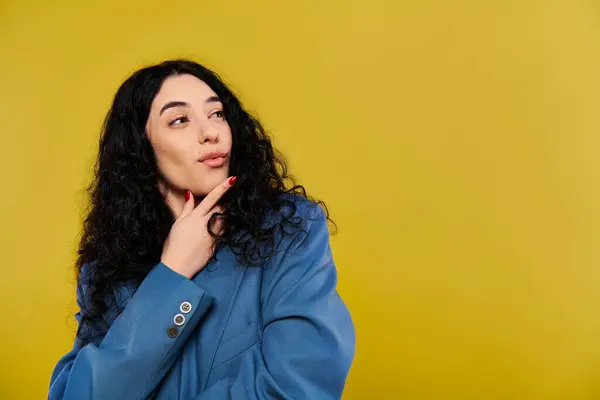 Une jeune femme aux cheveux bouclés vêtue d'une veste bleue respire l'élégance et l'émotion lorsqu'elle pose dans un studio au fond jaune. — Photo de stock