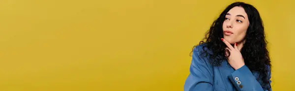 Jeune femme brune aux cheveux bouclés pose avec confiance dans une chemise bleue dans un studio avec un fond jaune vif. — Photo de stock