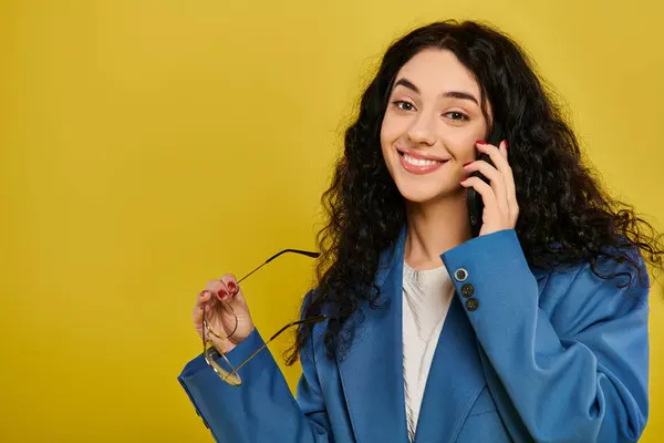 Une jeune femme brune dans une veste bleue élégante, parlant sur un téléphone portable avec un fond jaune. — Photo de stock
