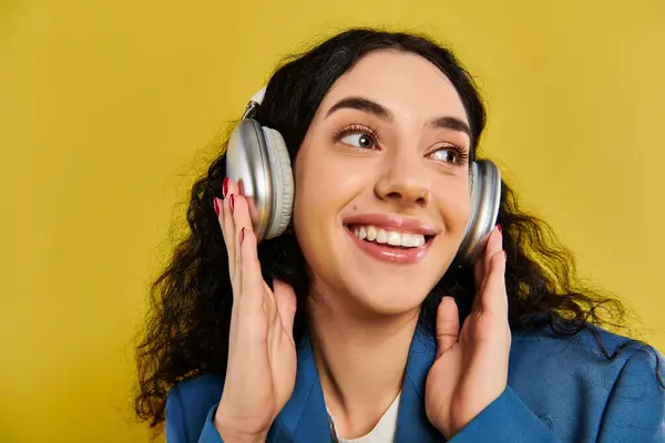 A young brunette woman with curly hair listens to music through headphones, lost in the rhythm against a vibrant yellow backdrop. — Stock Photo