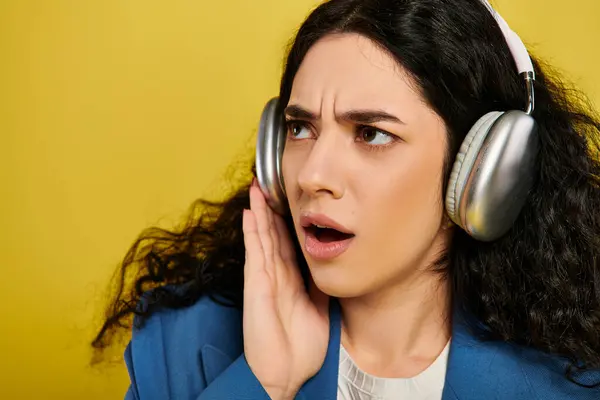 A brunette woman, headphones on, making a face, showcasing her emotions in a studio with a yellow background. — Stock Photo