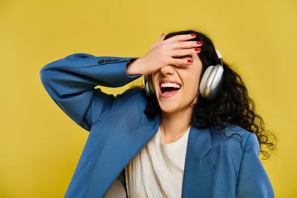 Uma jovem mulher com fones de ouvido cobrindo seus olhos, mostrando suas emoções em um traje elegante contra um pano de fundo amarelo. — Fotografia de Stock