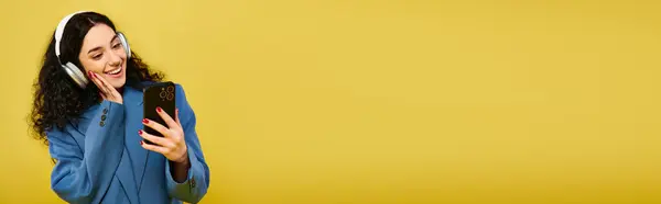 Une jeune femme brune aux cheveux bouclés portant un casque et parlant sur un téléphone portable, exprimant des émotions, dans un studio avec un fond jaune. — Photo de stock