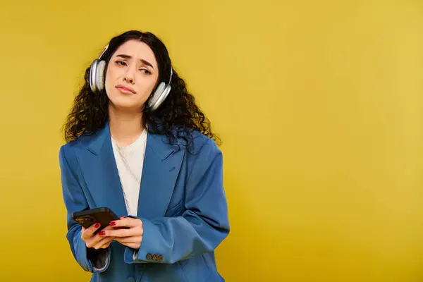 Une femme brune aux cheveux bouclés portant un casque et tenant un téléphone portable, perdue en musique sur fond jaune. — Photo de stock