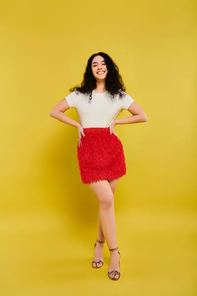 Brunette woman with curly hair striking a pose, showcasing emotions in a stylish red skirt against a yellow backdrop. — Stock Photo